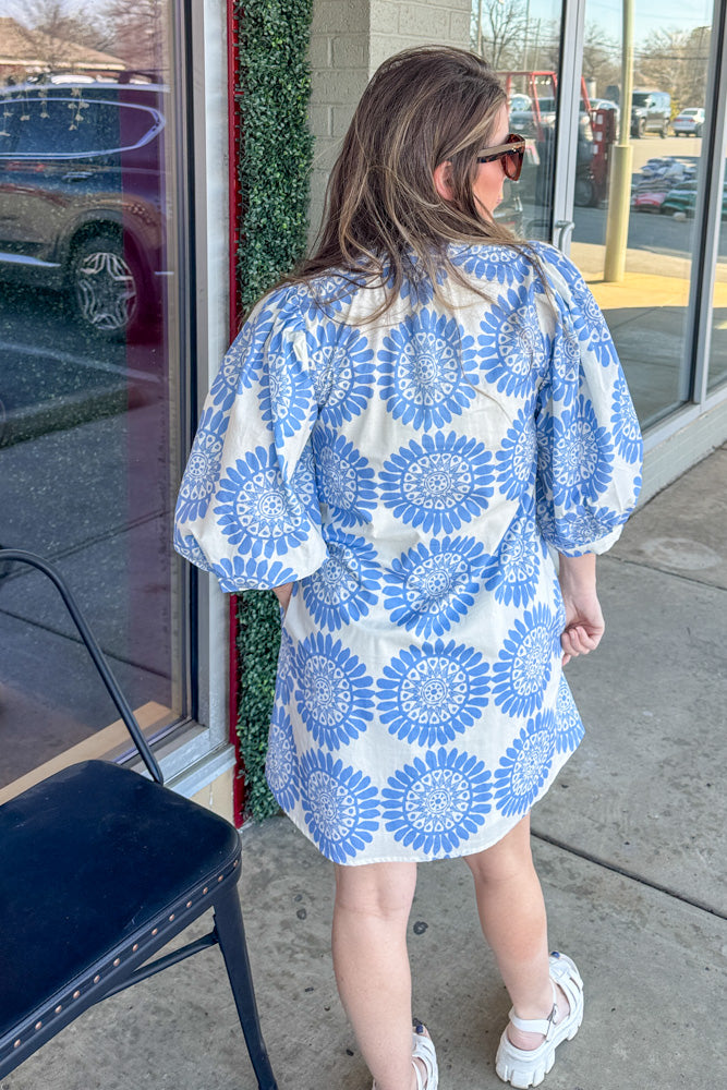 Woman wearing a blue and white floral dress standing outside a store.