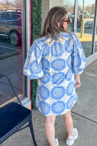 Woman wearing a blue and white floral dress standing outside a store.