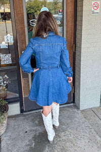 Person wearing a blue denim dress and white cowboy boots walking out of a building.
